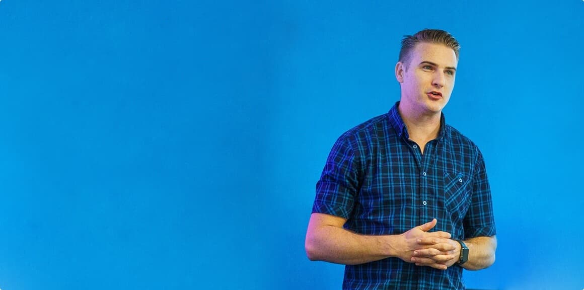 Professional man in blue plaid shirt presenting against vibrant blue background, representing Bluematter's healthcare consulting expertise Professional man in blue plaid shirt presenting against vibrant blue background, representing Bluematter's healthcare consulting expertise