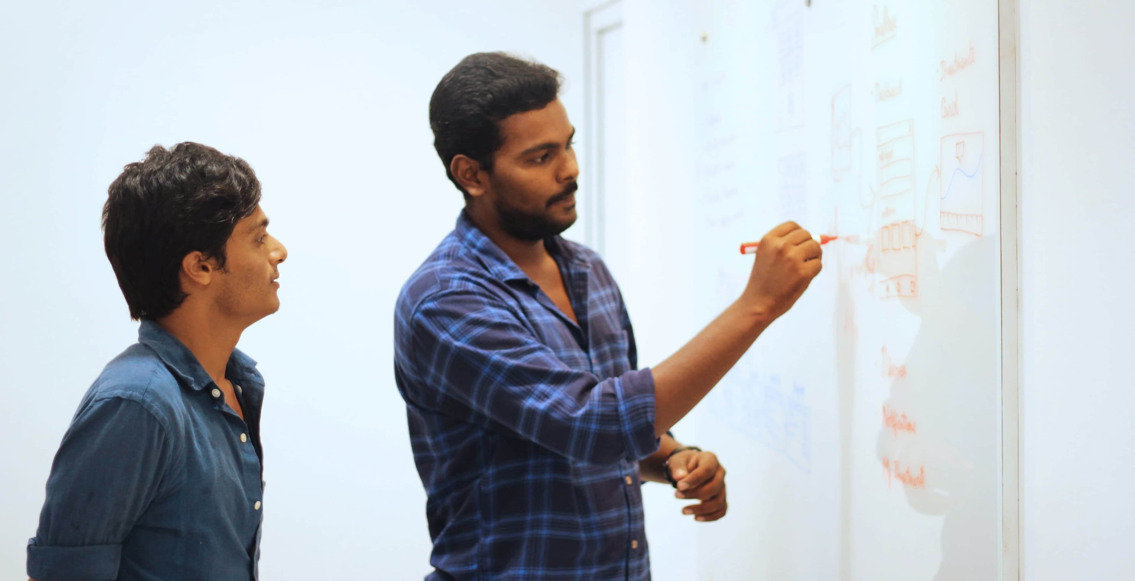 Two team members collaborating at a whiteboard, discussing design solutions with colorful sticky notes and sketches on the wall Two team members collaborating at a whiteboard, discussing design solutions with colorful sticky notes and sketches on the wall