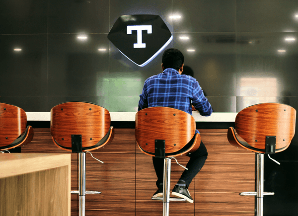 Employee working at standing desk bar with modern wooden high chairs and Timeless logo on glass wall Employee working at standing desk bar with modern wooden high chairs and Timeless logo on glass wall