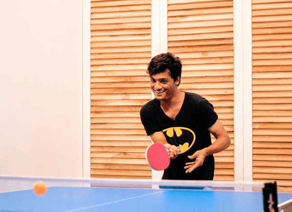 Team member playing table tennis in office recreation area wearing Batman t-shirt Team member playing table tennis in office recreation area wearing Batman t-shirt